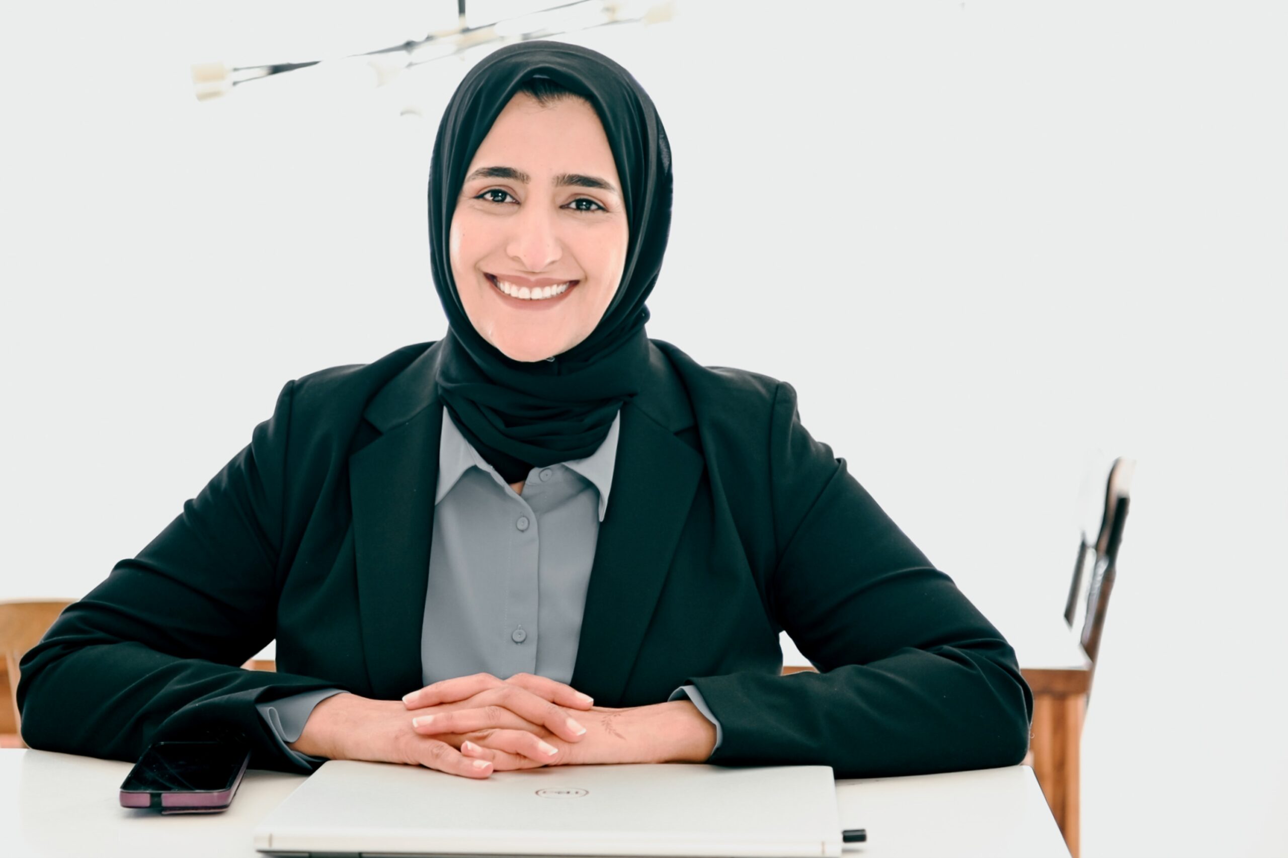 middle eastern woman smiling and seated in a chair with her hands folded together on a desk